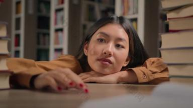 Tired pensive young asian woman lying on desk with books preparing for <strong>ex</strong>amination at university lib